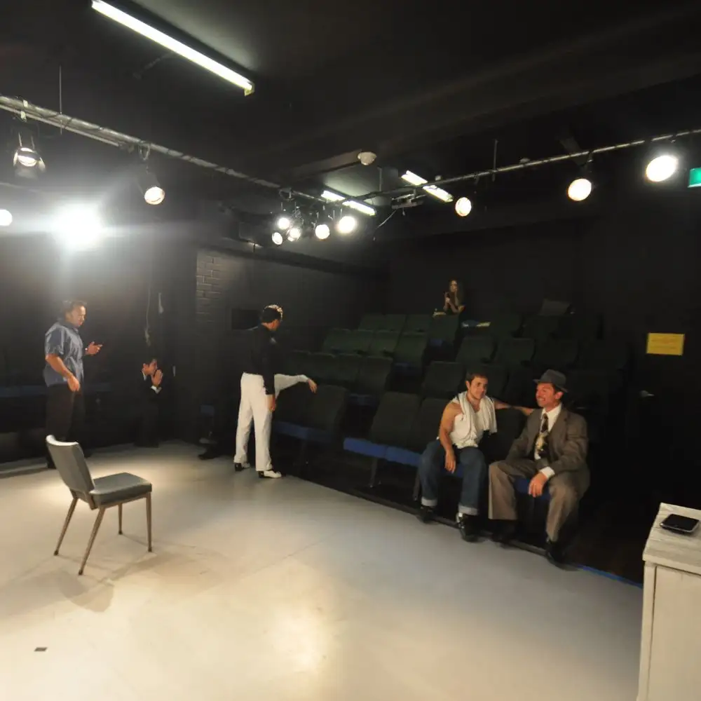 A photo of a small theater with people talking and sitting on tiered seating facing the stage.