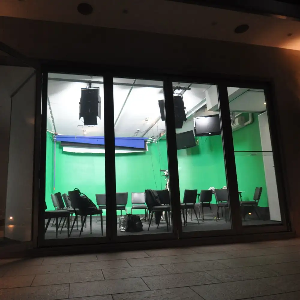 Photo of a room with green walls, chairs, tables, monitors, and overhead lights.