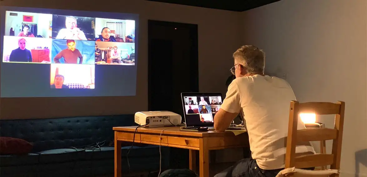 A photo of a man video conferencing on a laptop with a screen showing multiple people.