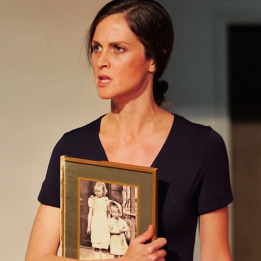 A woman in a dark dress holds a framed photo of two young children.