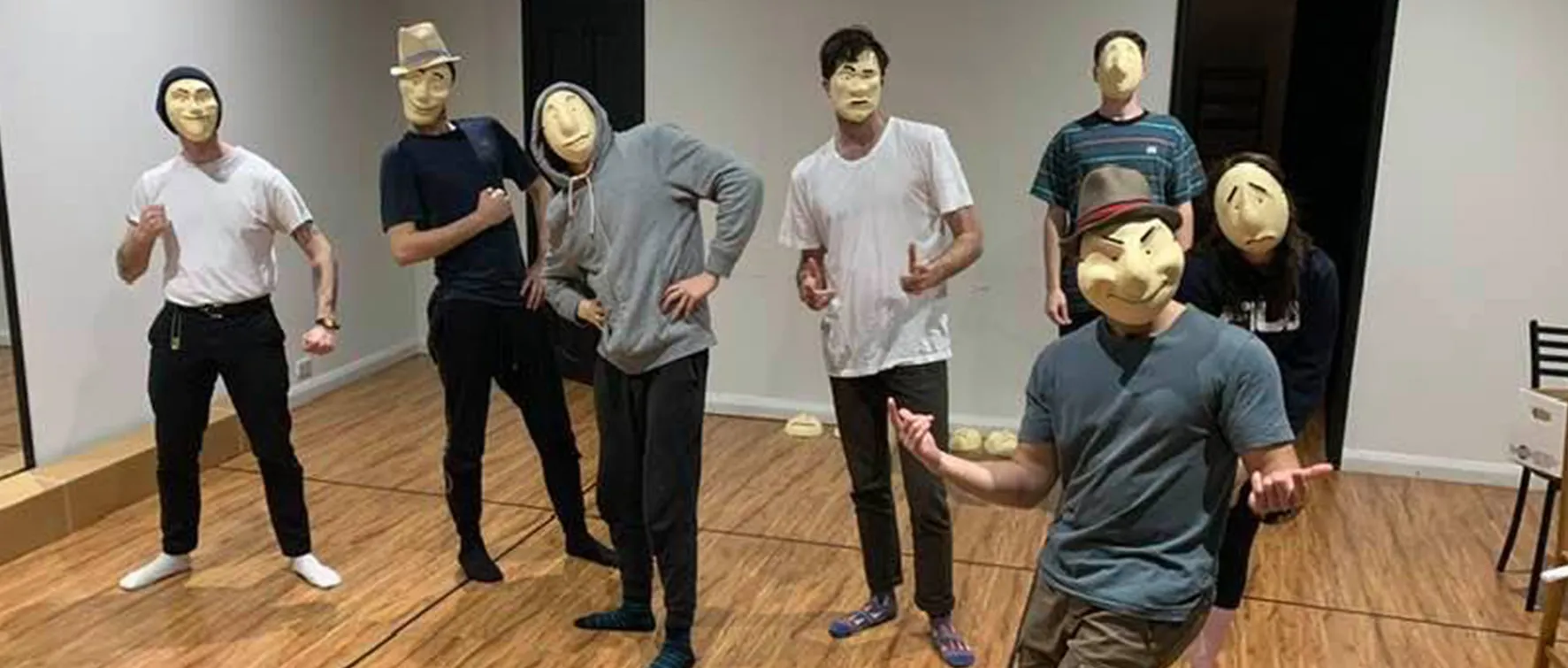A photo of seven people standing indoors, all wearing playful masks and casual clothing.
