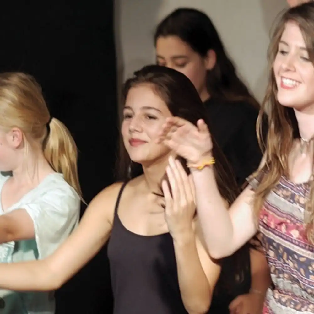 A photo of several smiling young people clapping and dancing together.