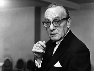 Black and white photo of an older man in glasses and a suit, looking at the camera.