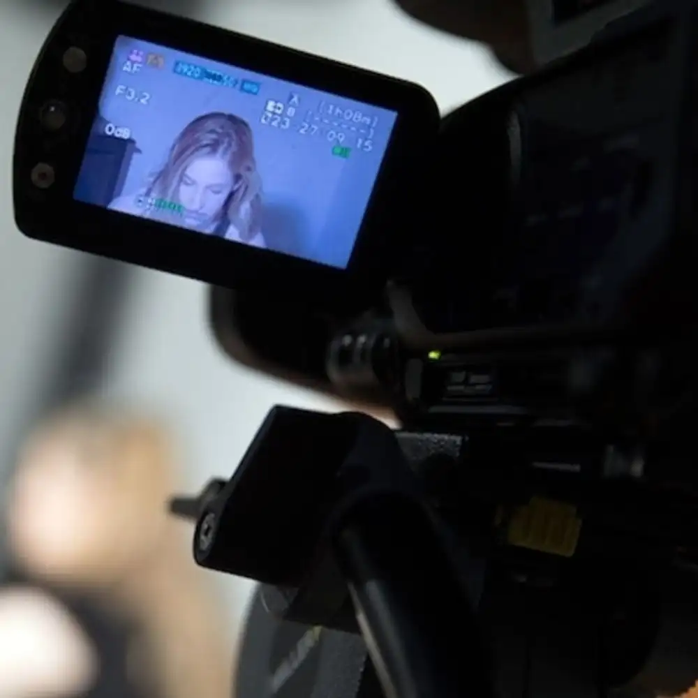 Photo of a camera filming a person, with the screen showing a woman in focus.