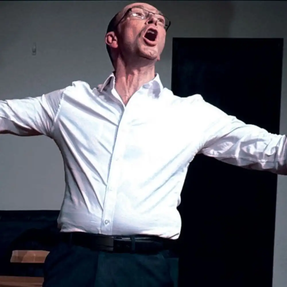 A man in a white shirt is singing passionately with arms outstretched.