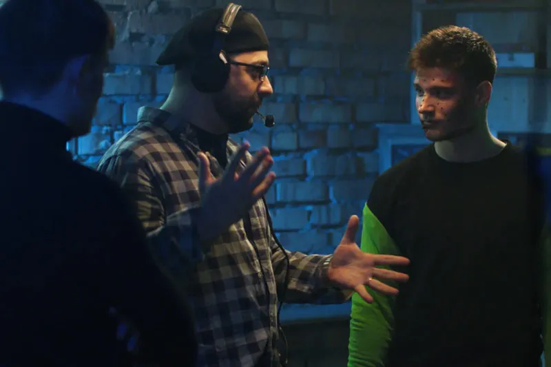 Three men in a dim room, one wearing a headset, likely discussing something.