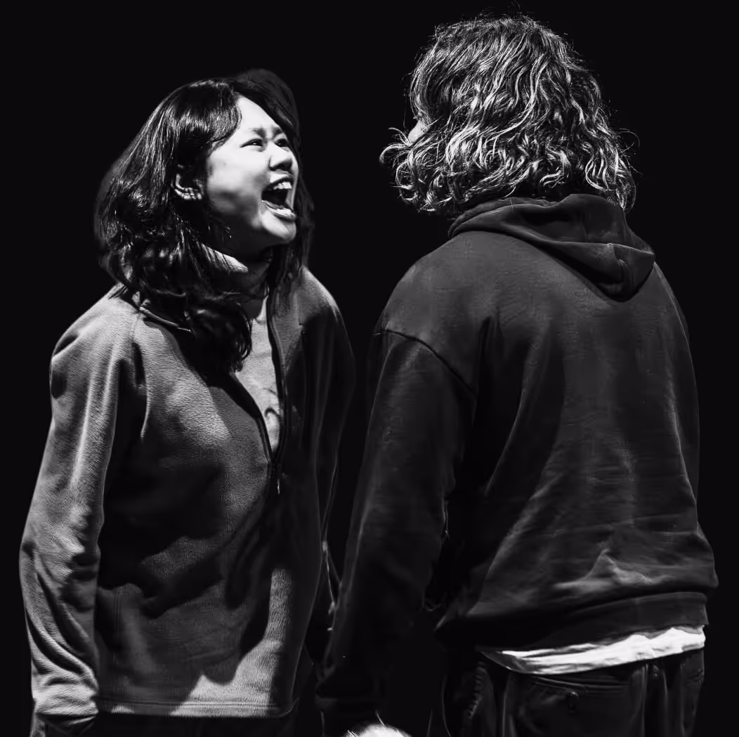 Black and white photo of two people facing each other, one laughing with mouth open.