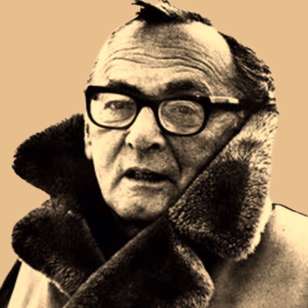 Older man wearing thick-rimmed glasses and a heavy fur-collared coat.