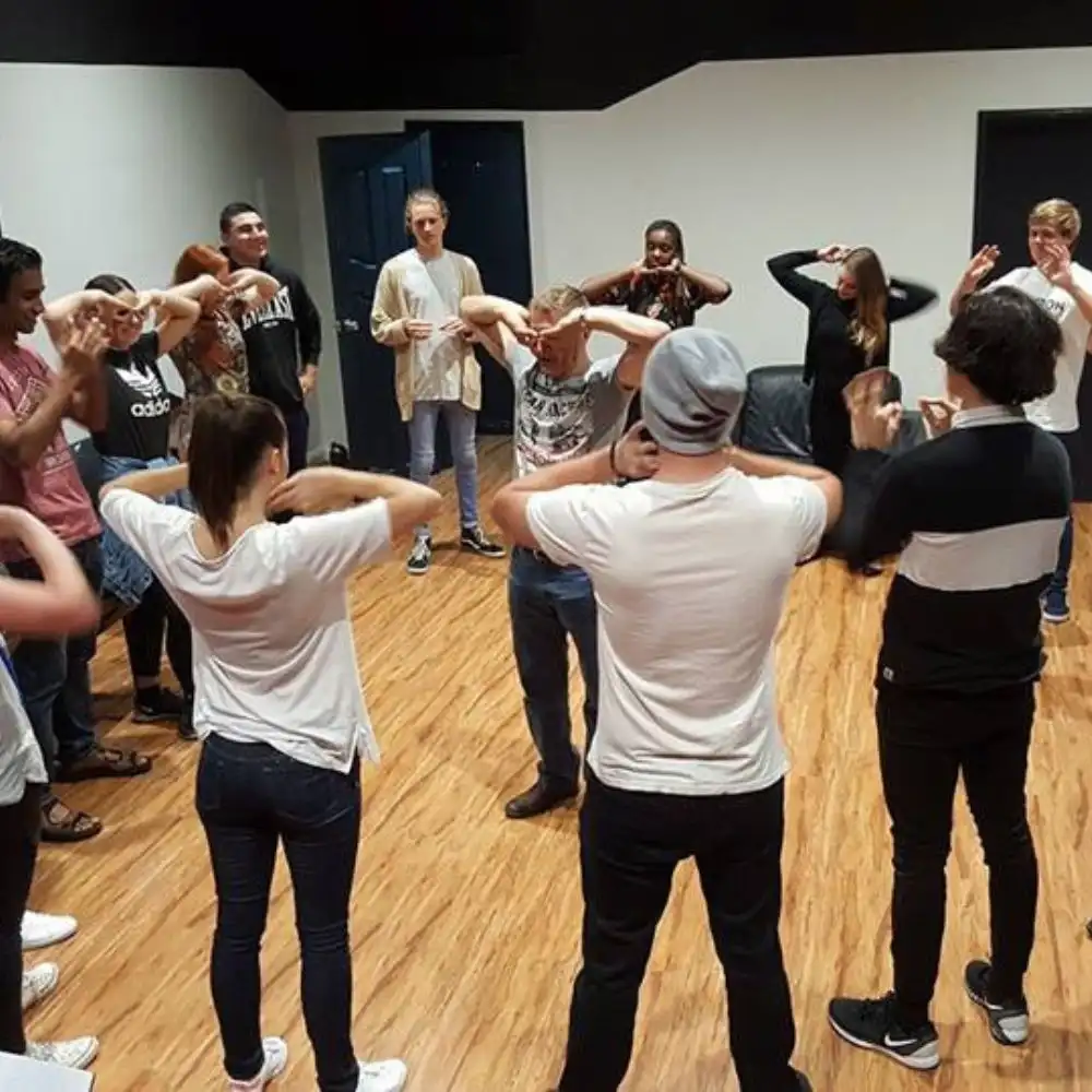 A photo of people gathered in a circle doing a group activity in a room.