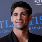 Portrait of a man with short dark hair and a slight smile wearing a black jacket at an event.