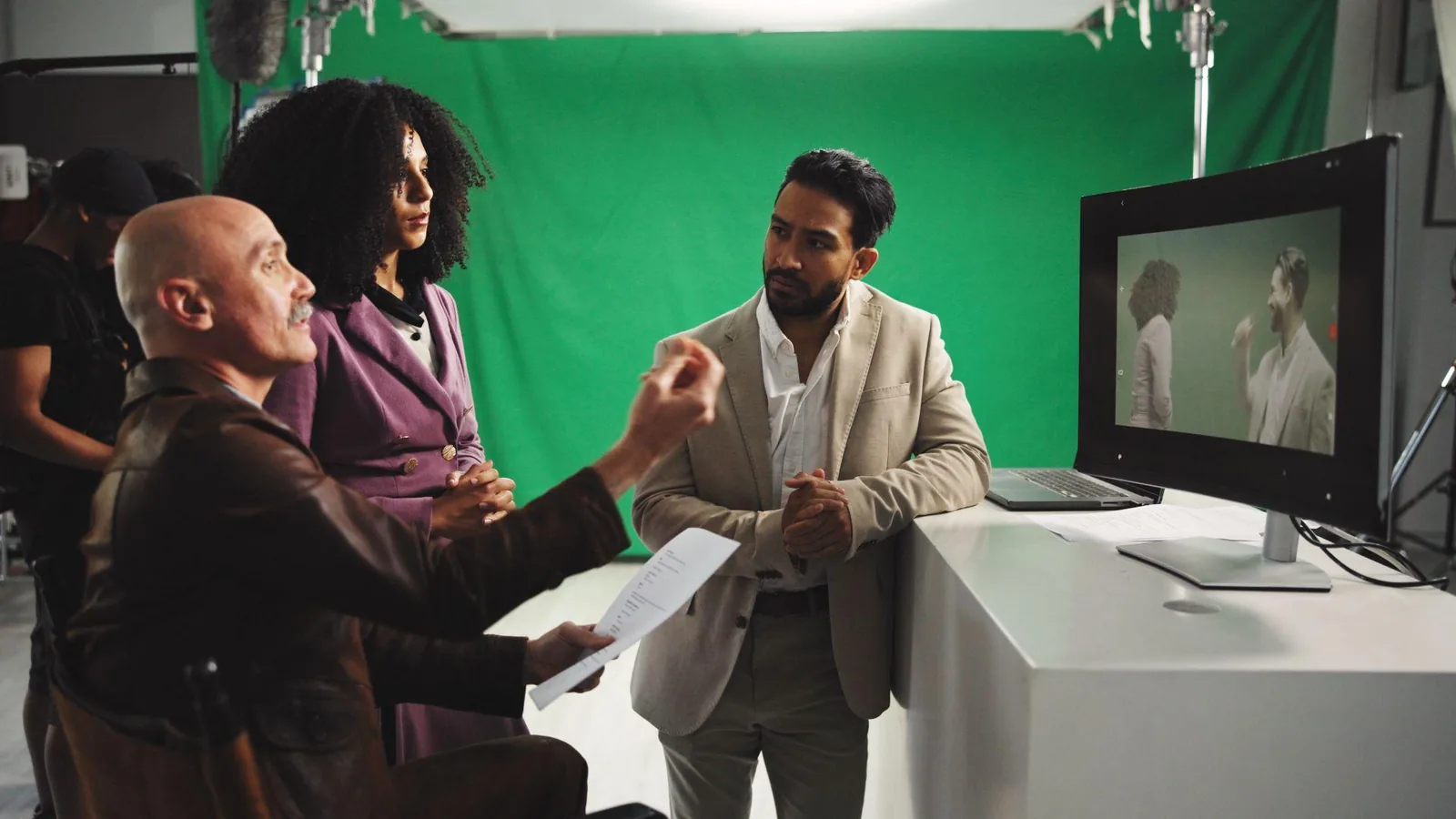 Actors and a director review a take on a studio monitor in front of a green screen